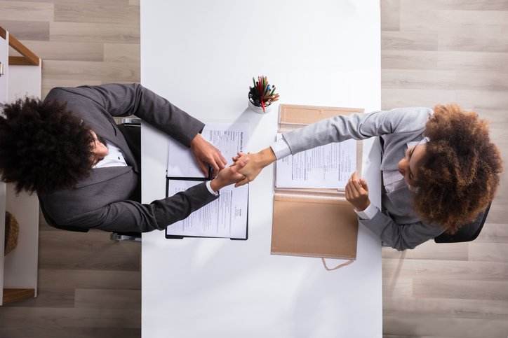 Overhead view of an interview handshake across a desk with resumes